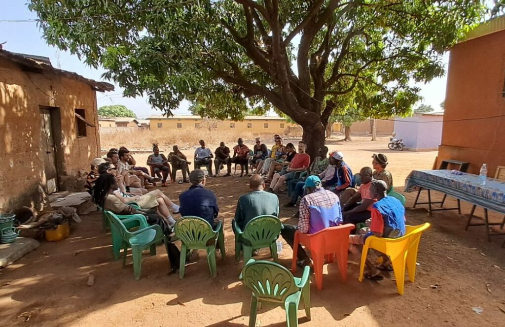 Stagiaires DIGIMONDE et musiciens ivoiriens en cercle de travail sous un manguier, formation afro-fusion à Korhogo, Côte d'Ivoire