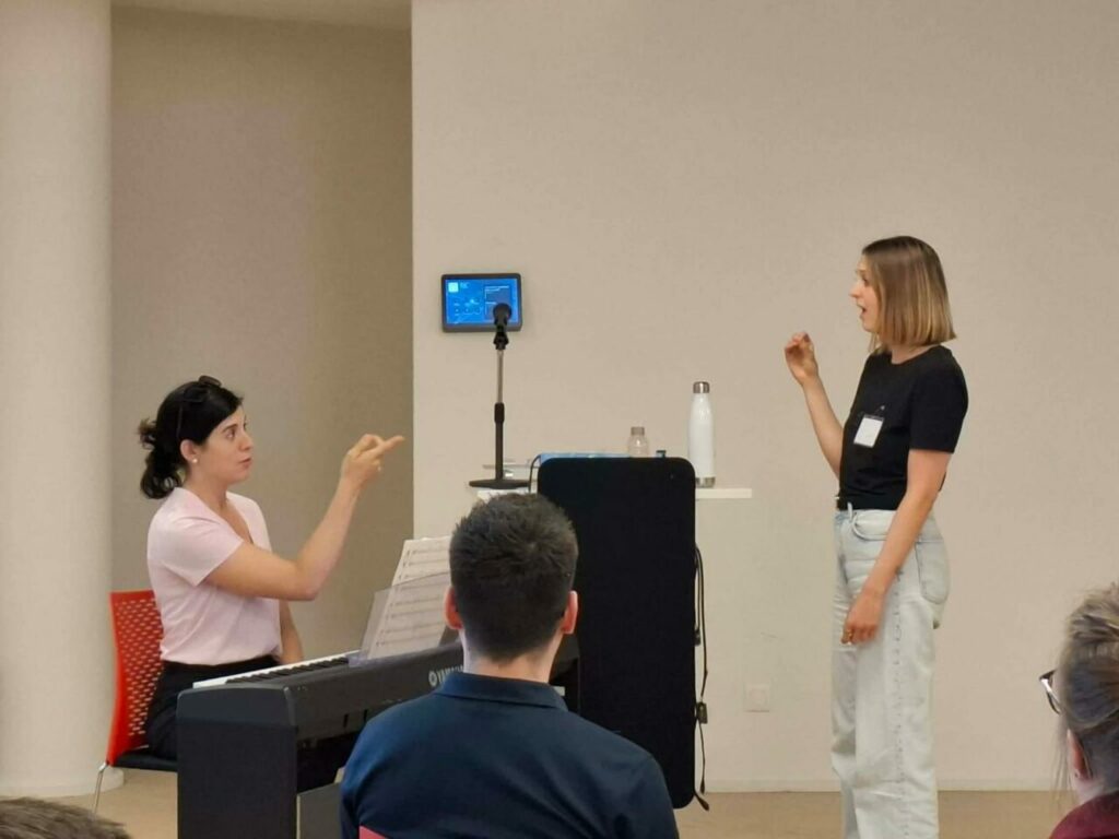 Paola Vera, coach vocale, accompagne une chanteuse devant les autres stagiaires