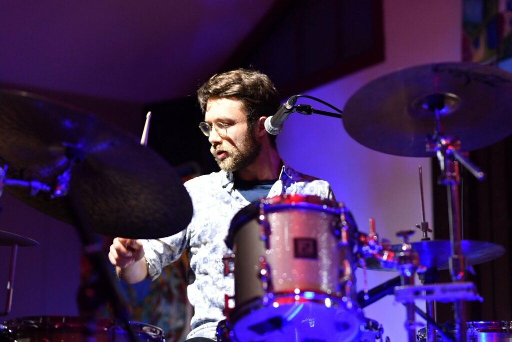 Simon Flouret à la batterie en concert, éclairage de scène bleu et rouge